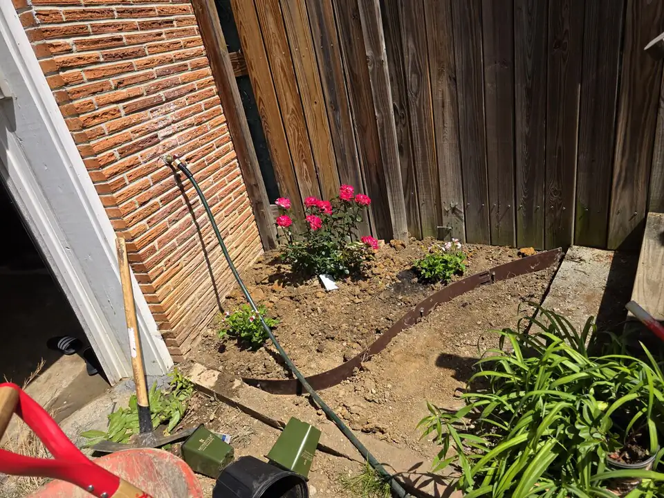 Before: a bare-dirt corner with garden tools, hose, and edging staged for a mulching job