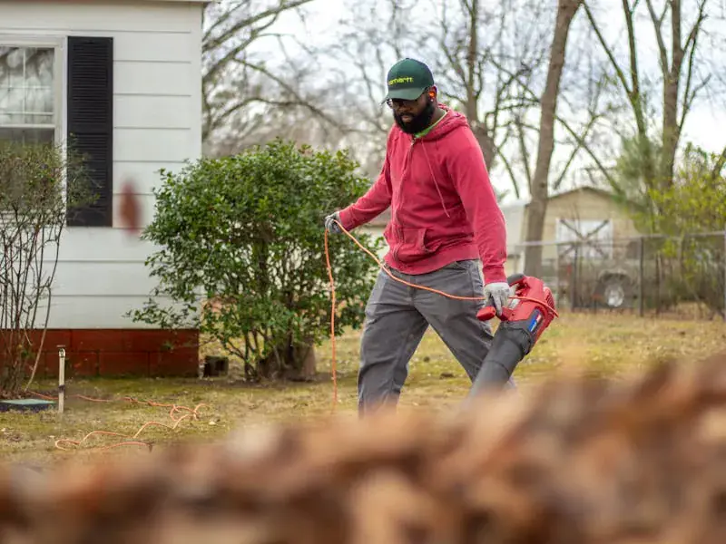 A worker using a leaf blower to clear leaves from a residential backyard — yard cleanup service.